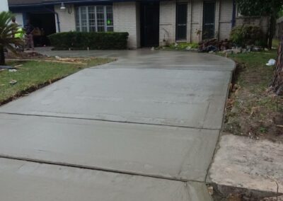 Freshly poured concrete driveway in front of a single-story home after renovation.